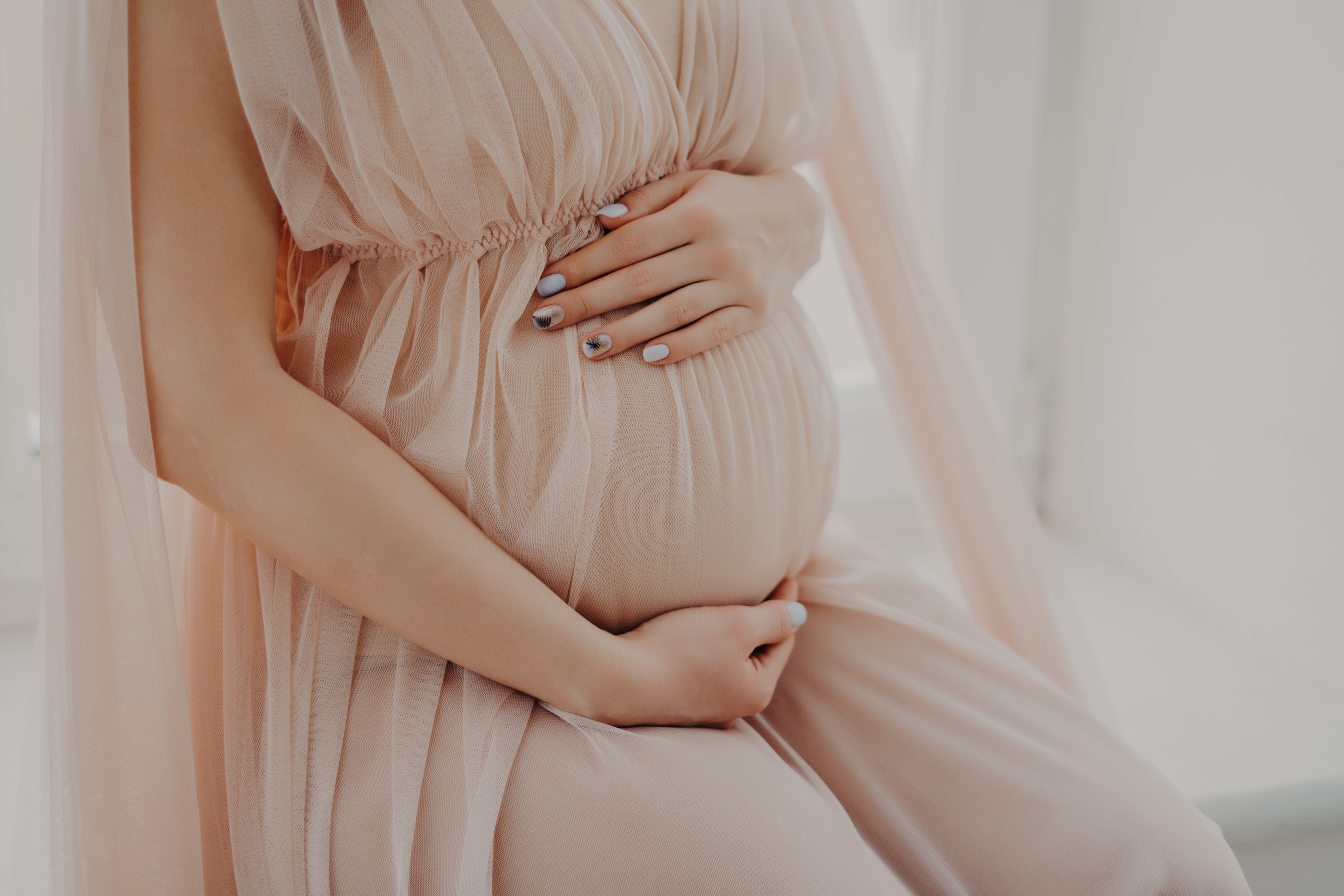 Cropped image of faceless woman touches her abdomen anticipates for baby wears festive dress poses indoor. Women and pregnancy concept
